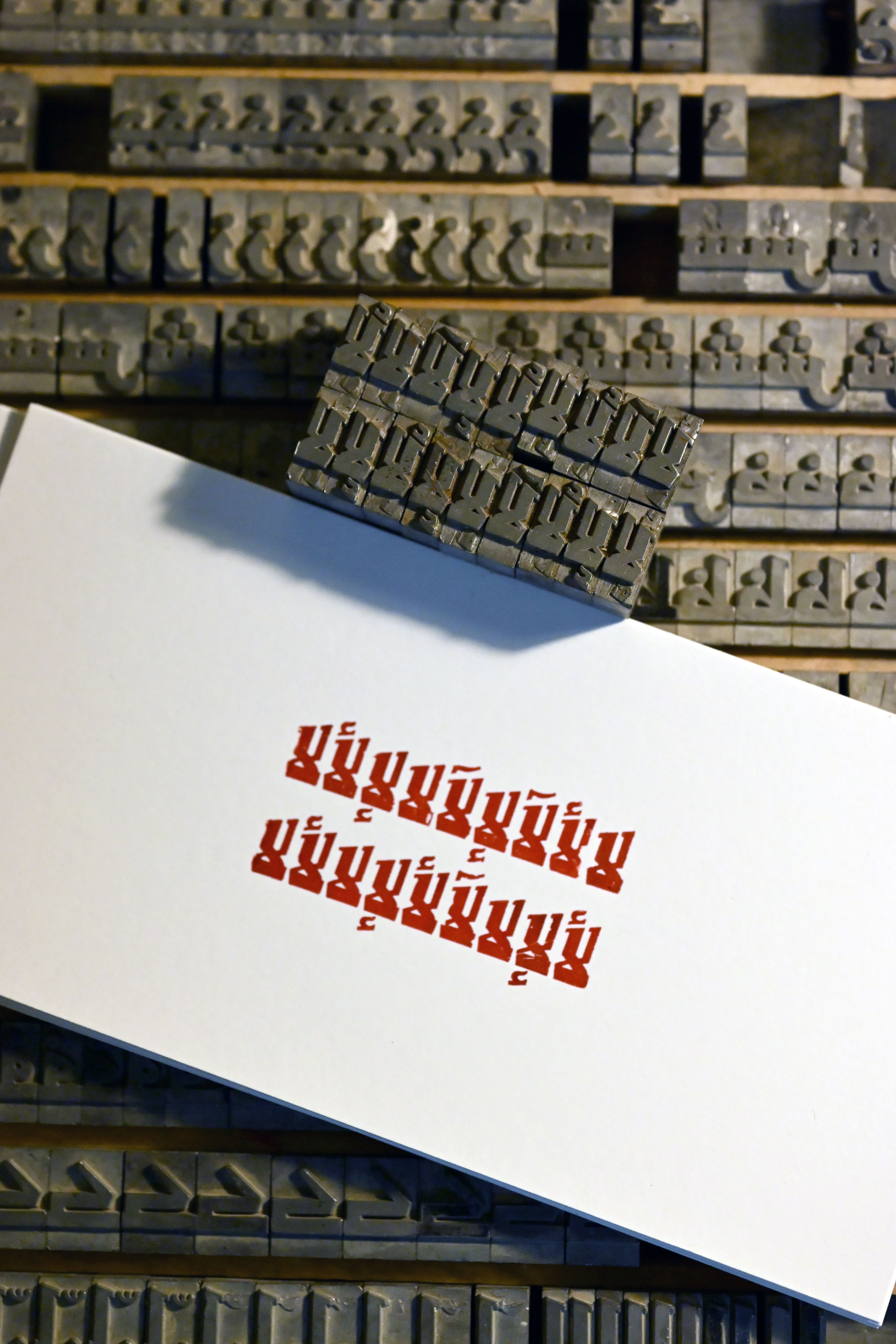 Metal movable type and a raised type block positioned over a white sheet printed with red Thai script.