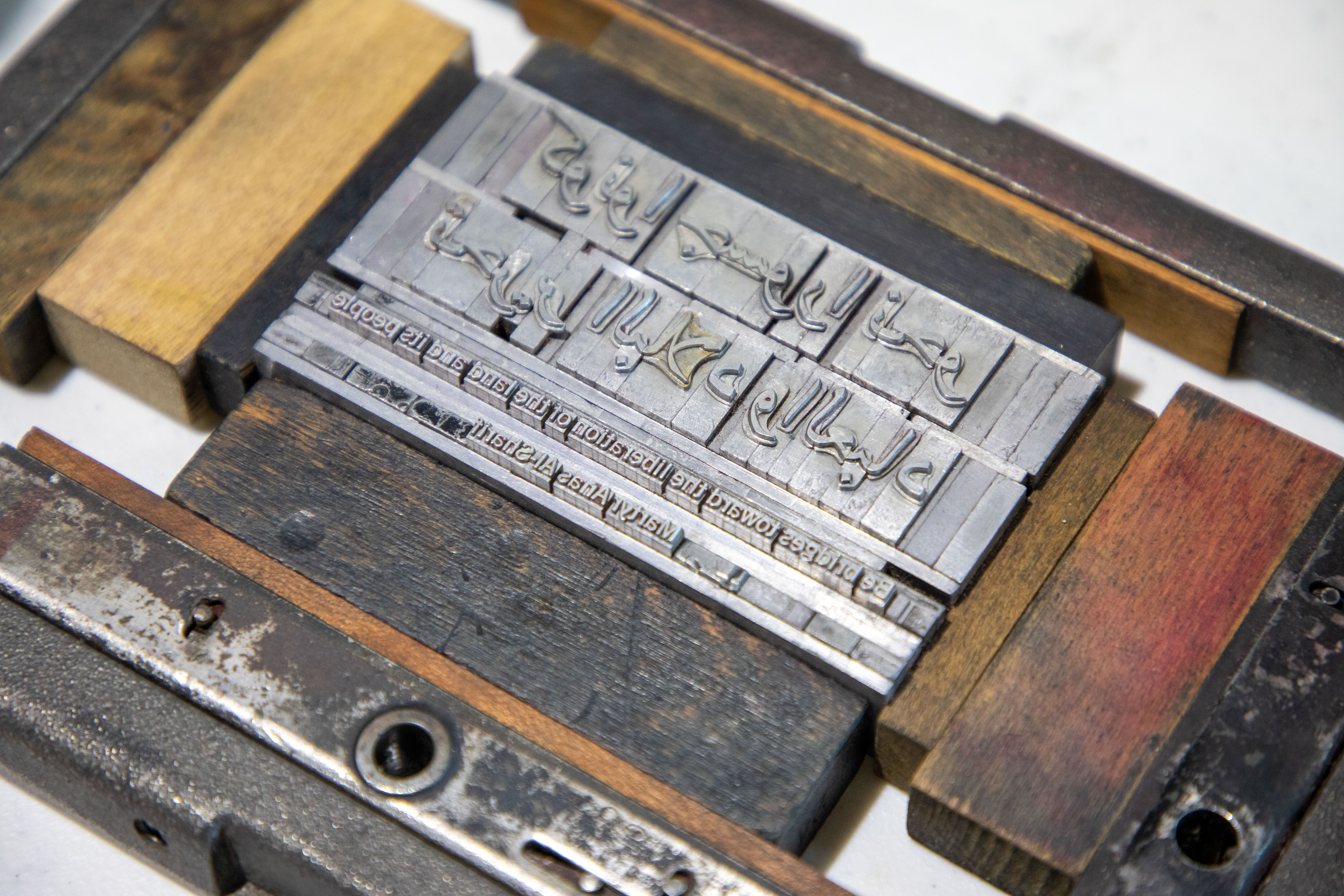 Close-up of raised Arabic-script metal printing type set in a worn wooden printing block.