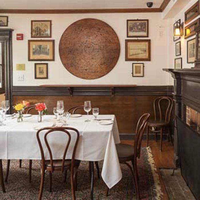 Image of Louis' Lounge at Mory's: a dining room with a set table, wooden chairs, wall art, and warm lighting.