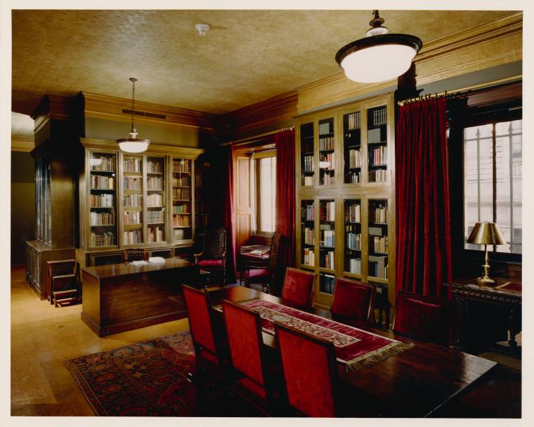 A classic library room with wooden furniture, red upholstery, and bookshelves filled with books.
